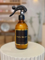 A room and fabric spray bottle with a cherry blossom label and a black spray nozzle, placed on a white surface.