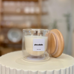 Candle in a glass jar with a wooden lid on a white surface, with a blurred background.