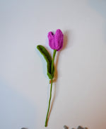 A handmade fabric flower with a purple petal and green stem laid out on a white surface.