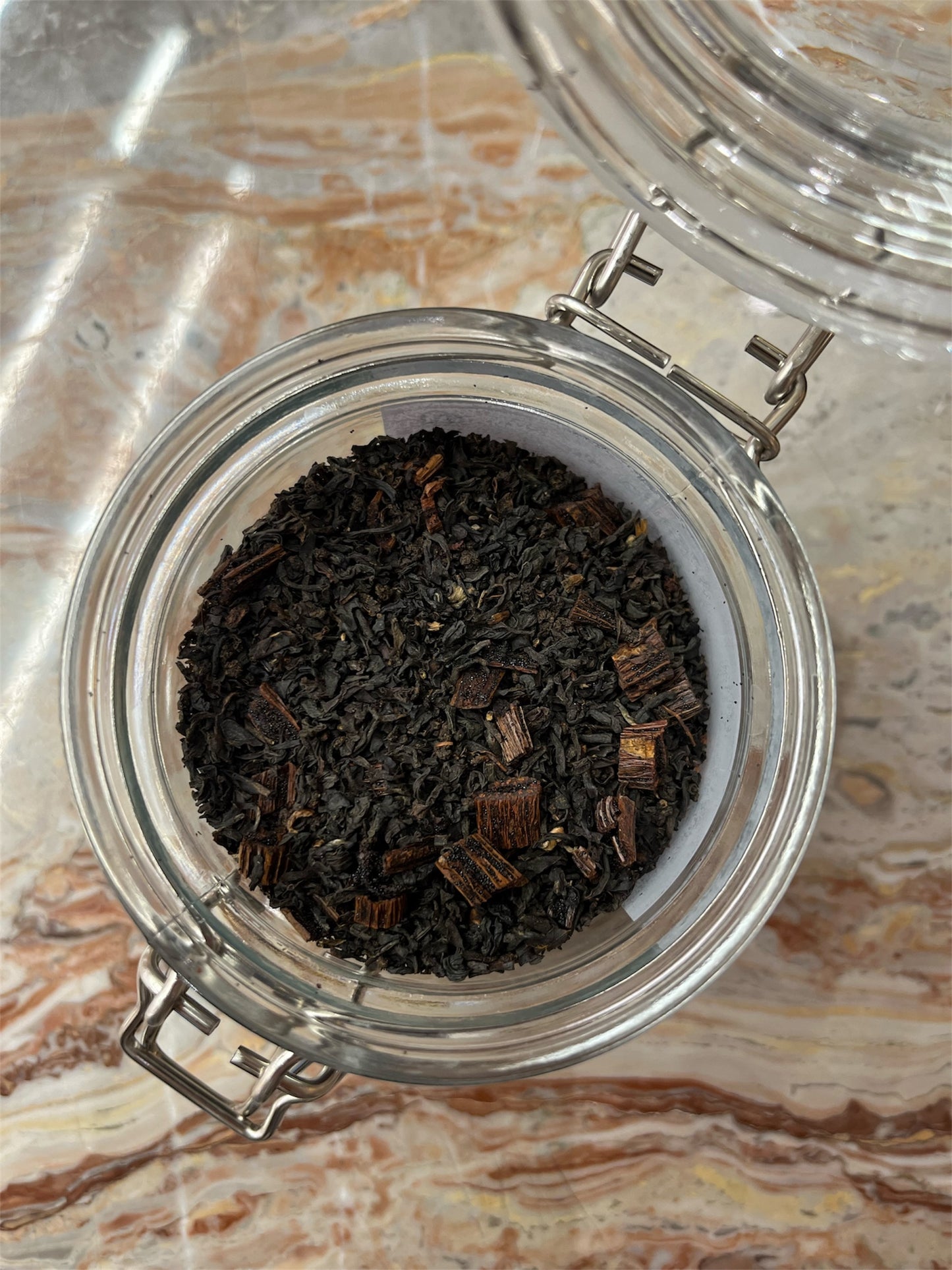 Glass jar with black tea leaves on a marble surface