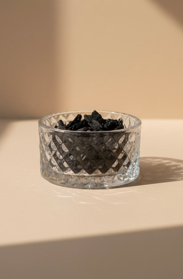 Clear glass bowl with black bakhoor on a beige surface