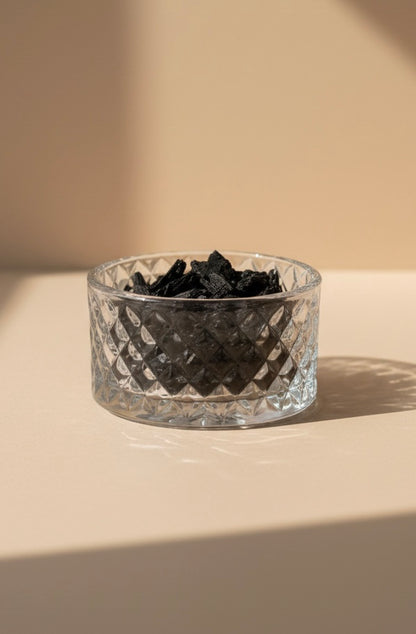 Clear glass bowl with black bakhoor on a beige surface