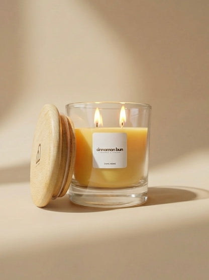 Glass candle with wooden lid labeled 'cinnamon bun' on a beige background