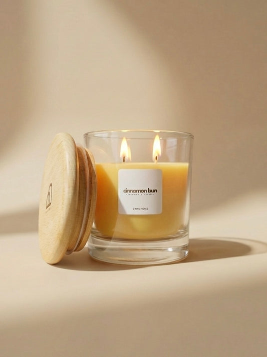 Glass candle with wooden lid labeled 'cinnamon bun' on a beige background
