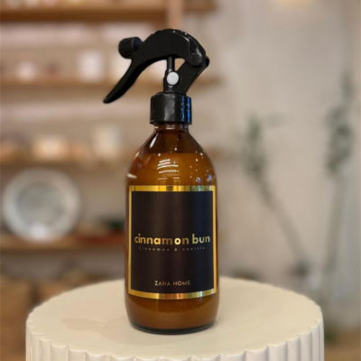 Brown spray bottle labeled 'cinnamon bun' on a white surface with a blurred background