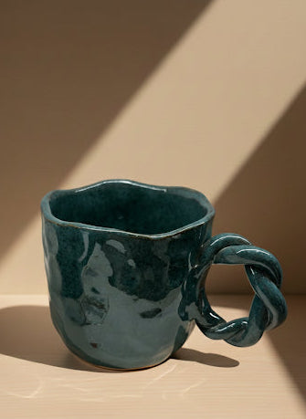 Teal ceramic mug with a unique handle design on a beige background