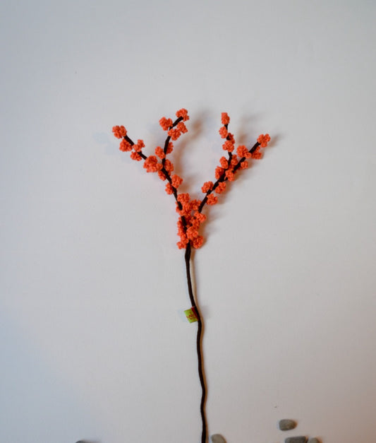 A handmade crochet flower with orange petals on a single stem against a white background.