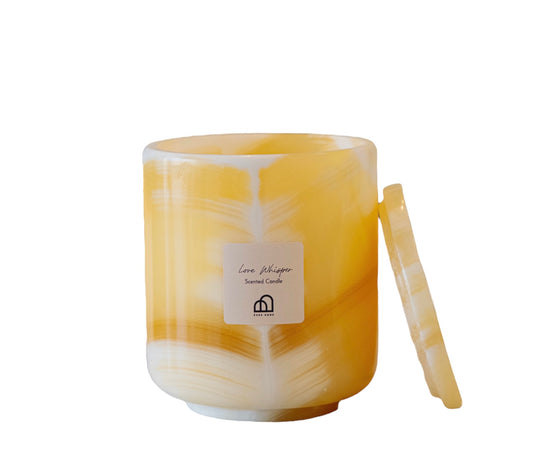 A translucent yellow-hued candle with a marble pattern, accompanied by a white wick, set in a clear onyx-like container with a white lid featuring a label.