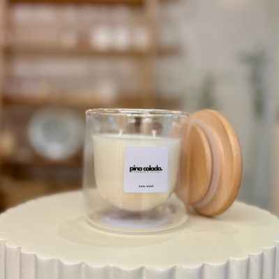 Candle in a glass jar with a wooden lid on a white surface, with a blurred background.