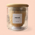 Glass candle with wooden lid and 'rose oud' label on a pink background